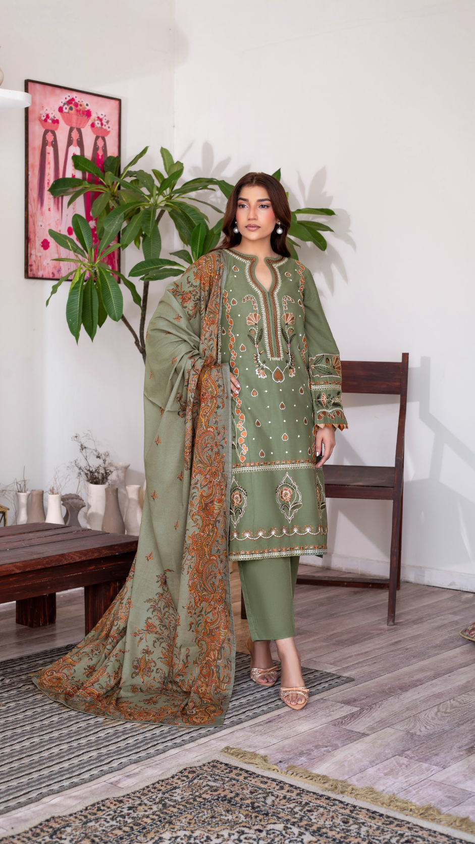 A woman wearing an elegant olive-green embroidered traditional outfit with a patterned dupatta.